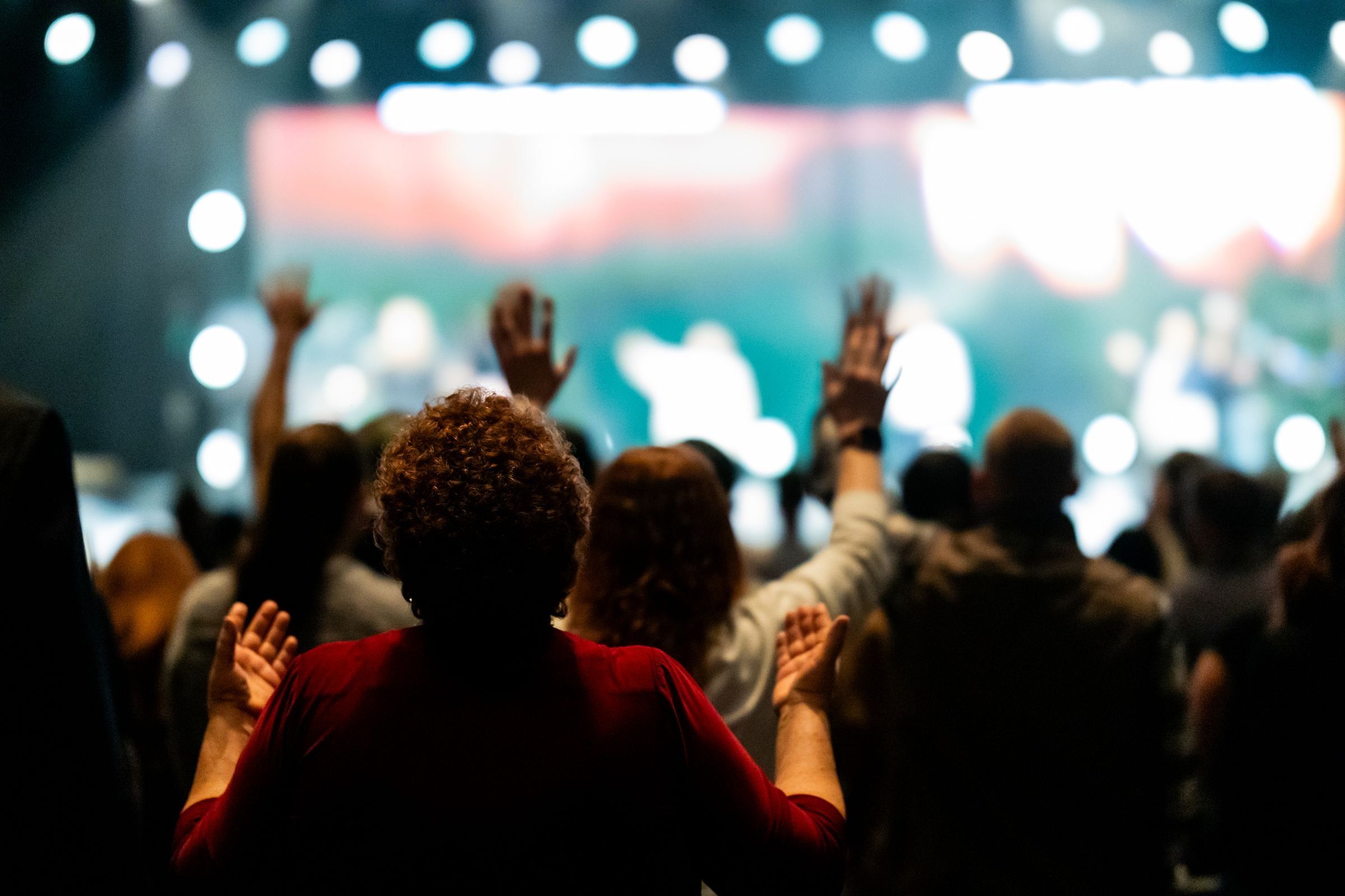 People with raised hands facing a lit stage