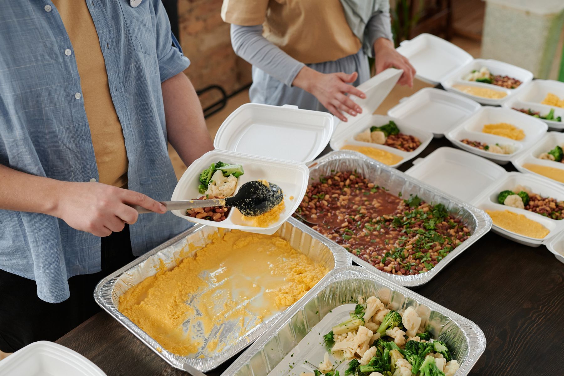 Volunteers serving beans, vegetables, and cornbread into take-away trays